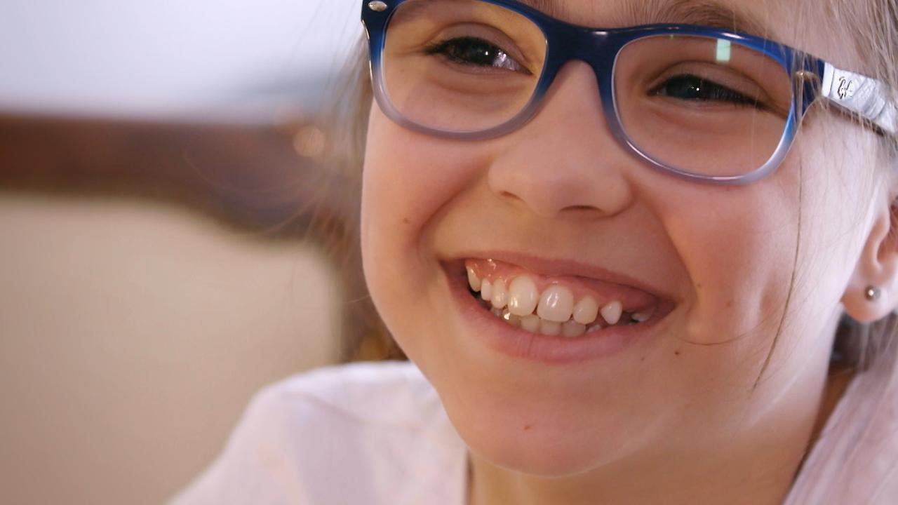 Auf diesem Bild ist fast nur Hannahs Gesicht zu sehen sowie ein Teil ihrer Schultern. Sie lacht sehr offen und fröhlich, trägt eine Brille mit blauem Gestell und eine weiße Bluse.