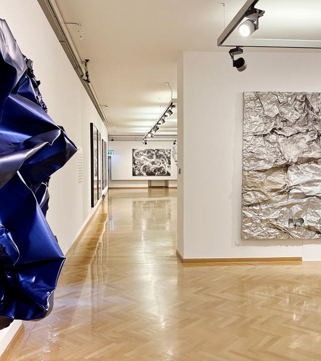 Zerknautschte Wandbilder aus Aluminium hängen in einem Ausstellungsraum