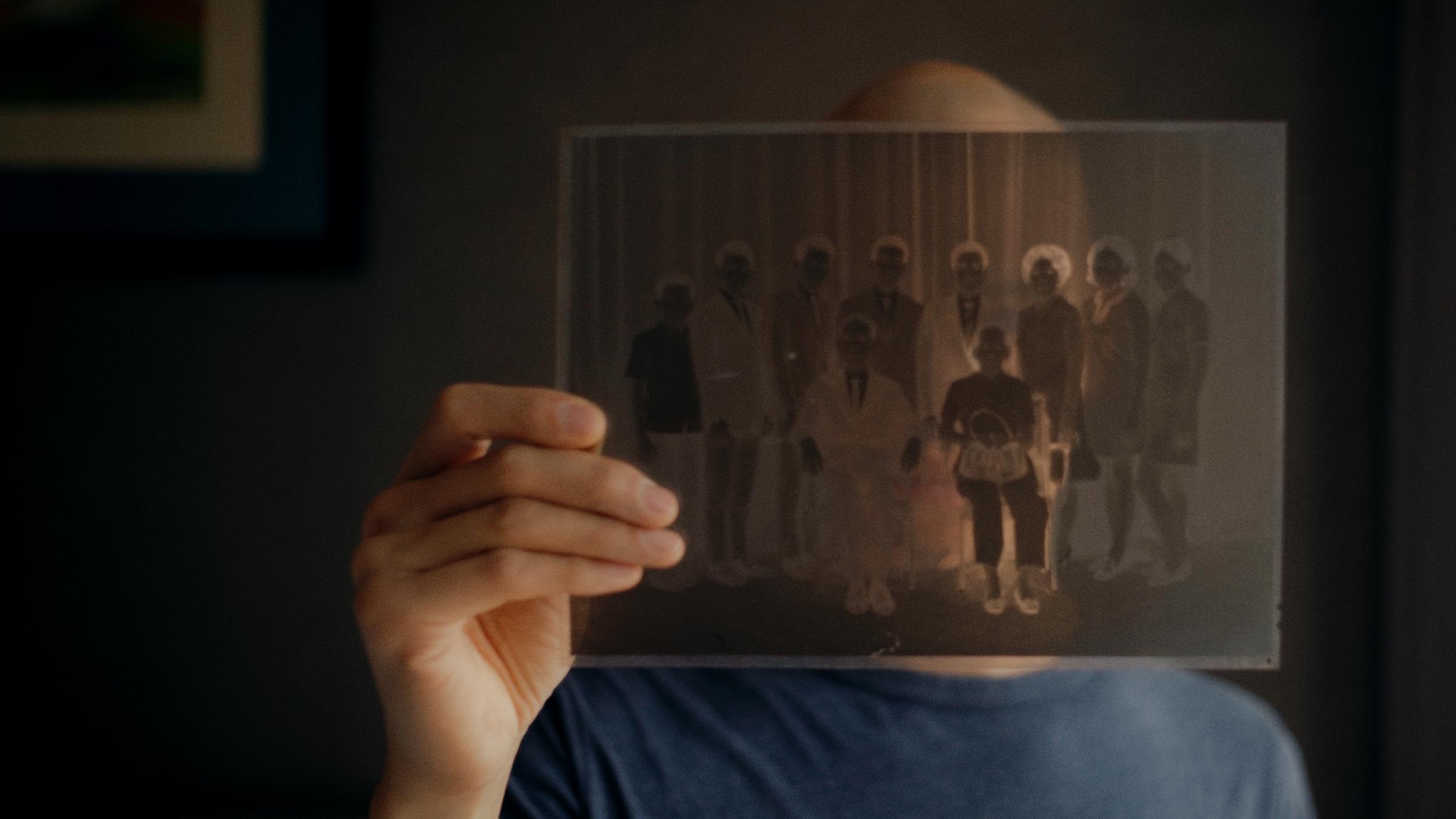 "Hao Are You": Regisseur Dieu Hao Do in einer Nahaufnahme. Er blickt durch ein Negativ eines Familienfotos, welches er in seiner Hand hält.