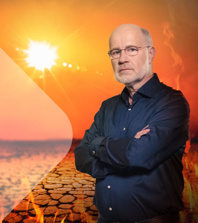Harald Lesch steht bei gleißender Sonne auf ausgetrockneter Erde