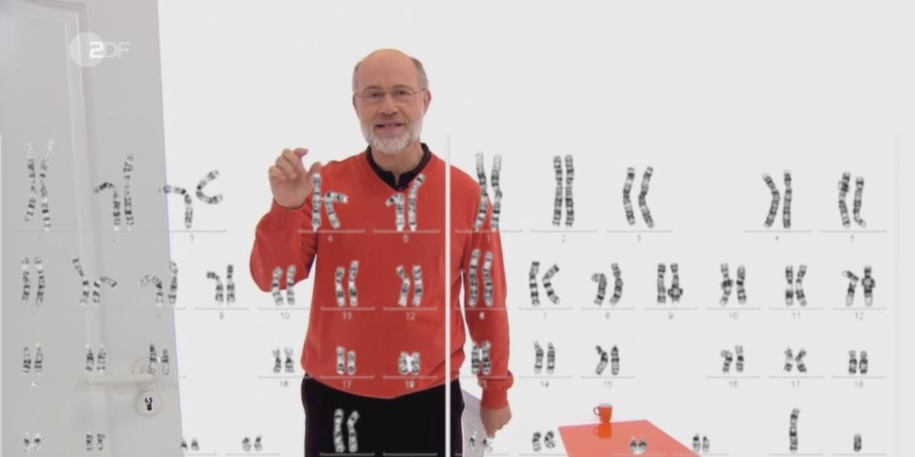 Harald Lesch hinter einer Tafel mit Abbildung von Genen