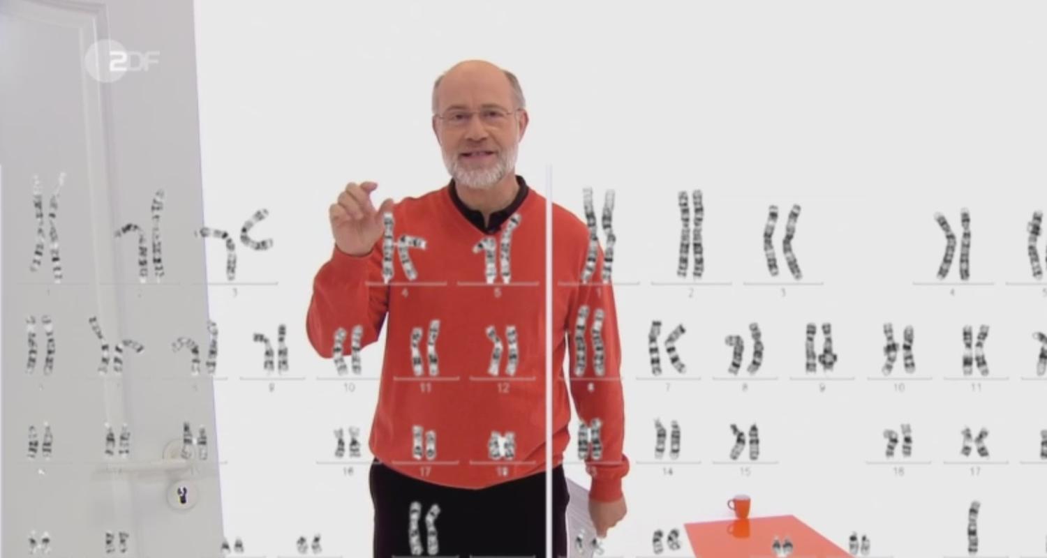 Harald Lesch hinter einer Tafel mit Abbildung von Genen