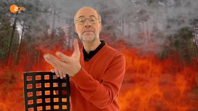 Harald Lesch vor einem virtuellen Waldbrand in seinem Studio