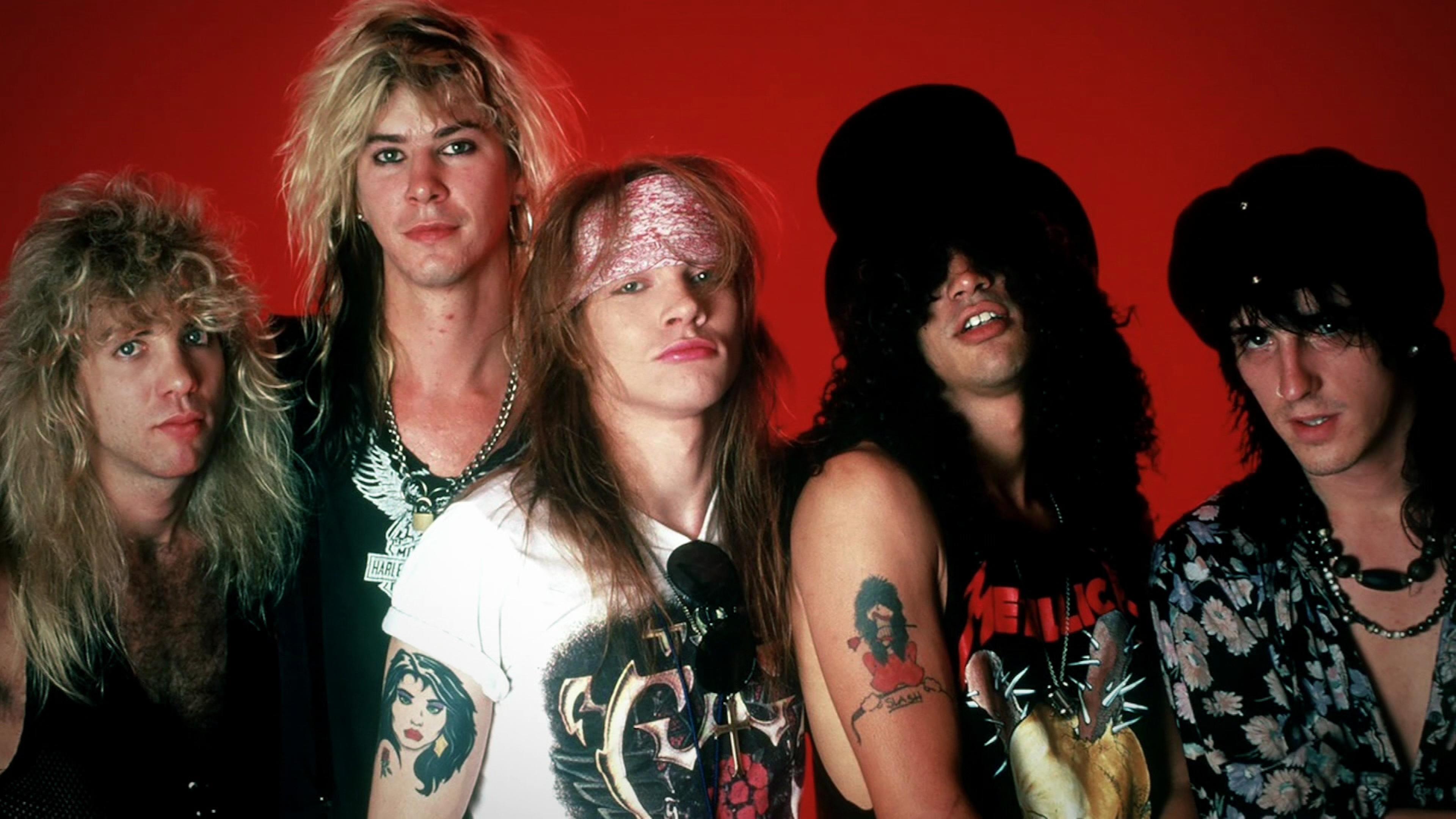 Fünf Musiker von Guns N' Roses, mit längeren Haaren und Tattoos schauen in die Kamera.