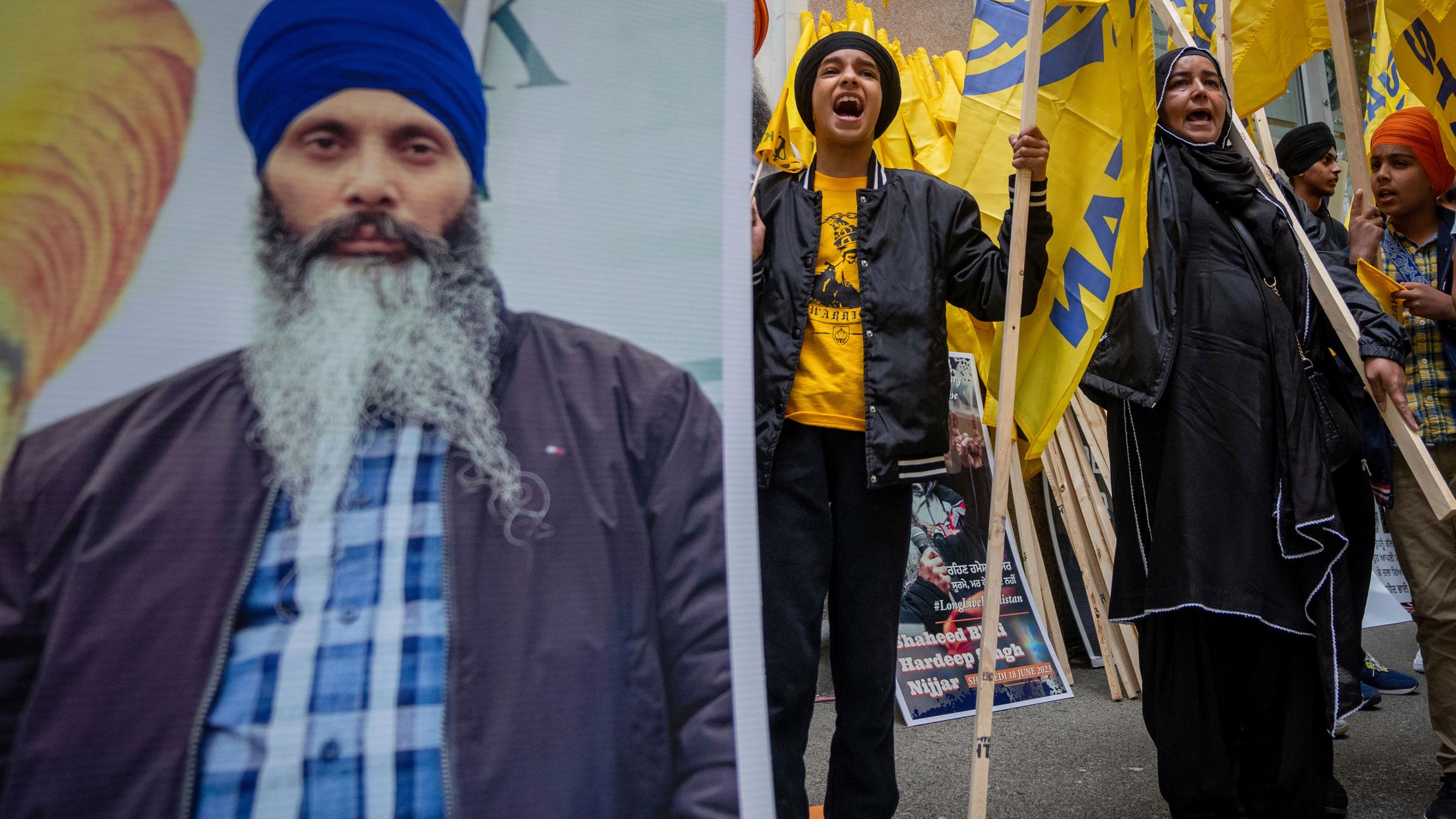 A large poster features a portrait of Hardeep Singh Nijjar, while several people protest in the background.