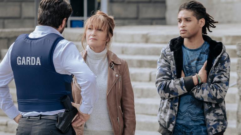 "Harry Wild - Mörderjagd in Dublin: Einer wird gewinnen": Harry Wild (Jane Seymour) im Gespräch mit einem uniformierten Polizisten, ihr Sohn Charlie (Kevin J. Ryan). Neben ihr steht Fergus (Rohan Nedd).