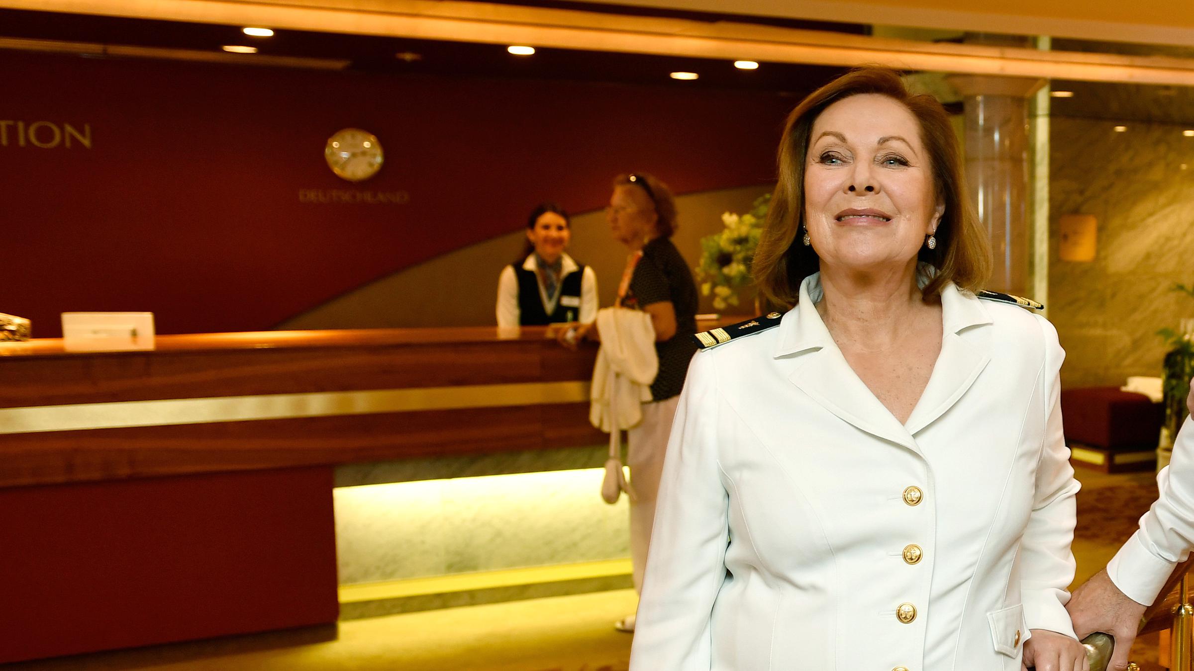 Beatrice (Heide Keller) steht am inneren Treppenaufgang im Schiff. Im Hintergrund sieht man die Rezeption des Schiffs.