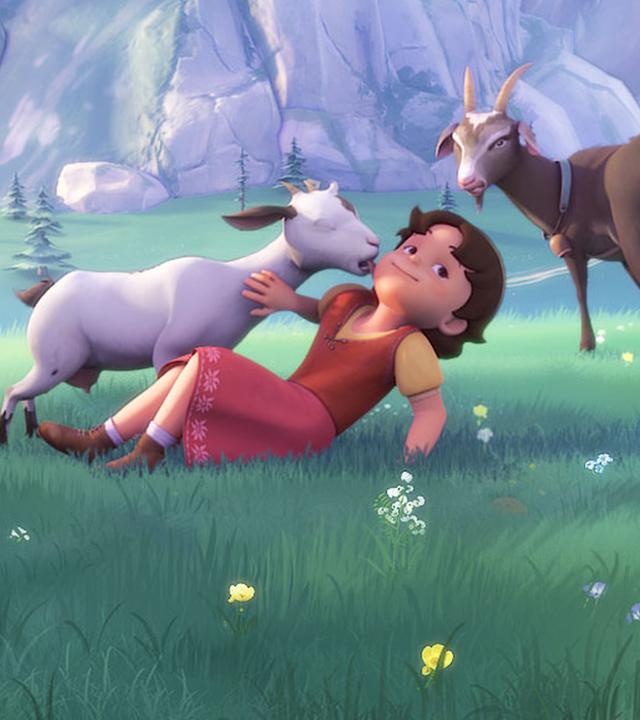 Heidi spielt auf einer Wiese mit Ziegen. Dabei schleckt ihr eine Ziege das Gesicht ab.