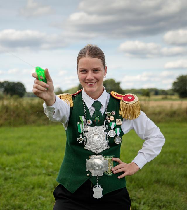 Anneke steht mit einer Wasserspritzpistole in der Hand auf einem Feld und drückt ab.