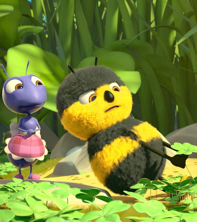 Heini Hummel steht in einer Kleeblatt-Wiese und zieht mit aller Kraft an einem vierblättrigen Kleeblatt. Anna Ameise steht links neben ihm und sieht ihm dabei zu.