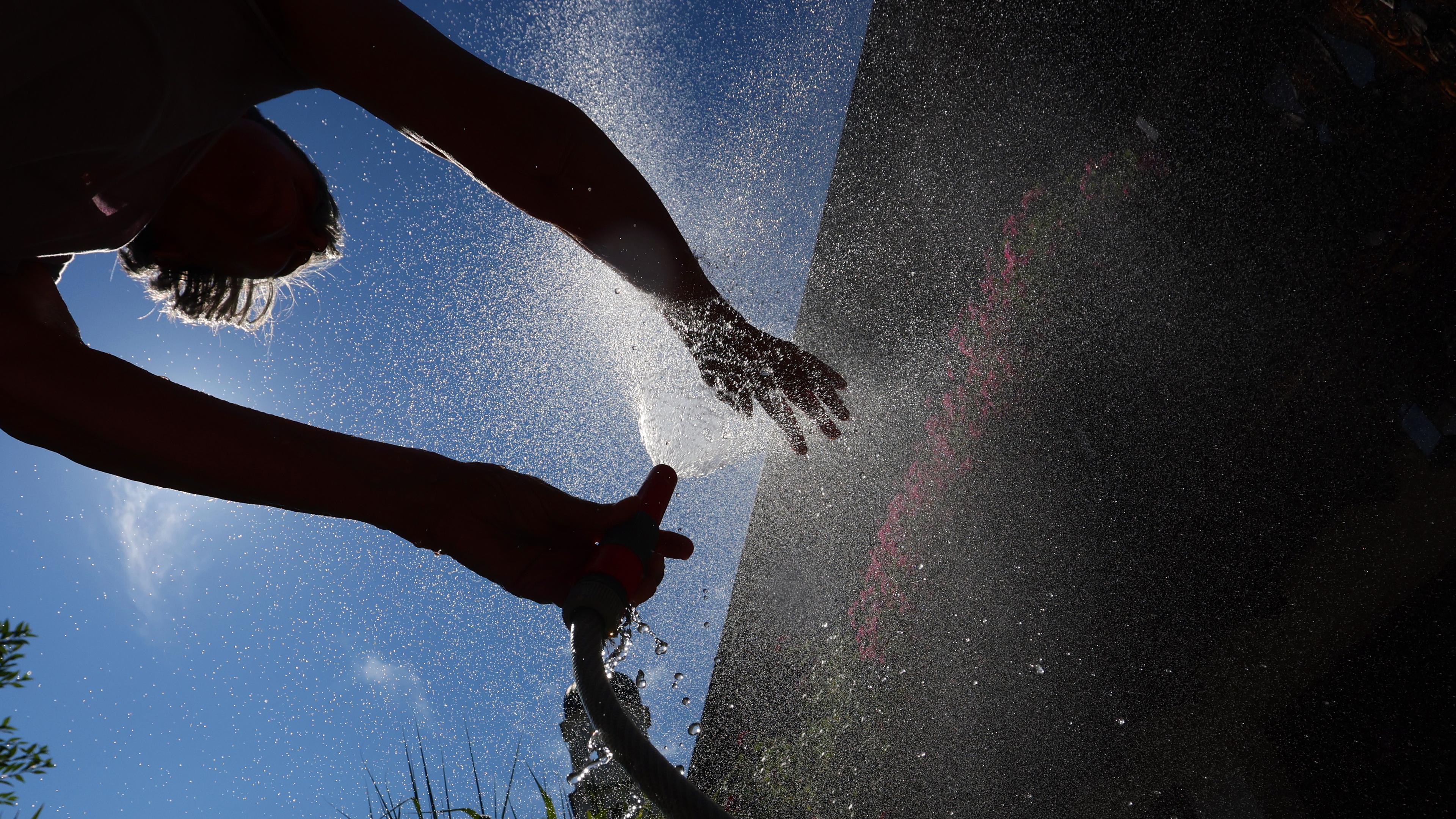 Bayern, Kaufbeuren: Ein Frau kühlt sich in einem Garten mit Wasser aus einem Gartenschlauch ab.