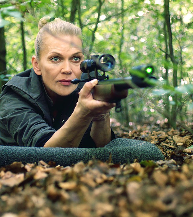 "Helen Dorn - Das Recht zu schweigen": Helen Dorn (Anna Loos) liegt bäuchlings mit einem Gewehr im Anschlag auf dem Waldboden.