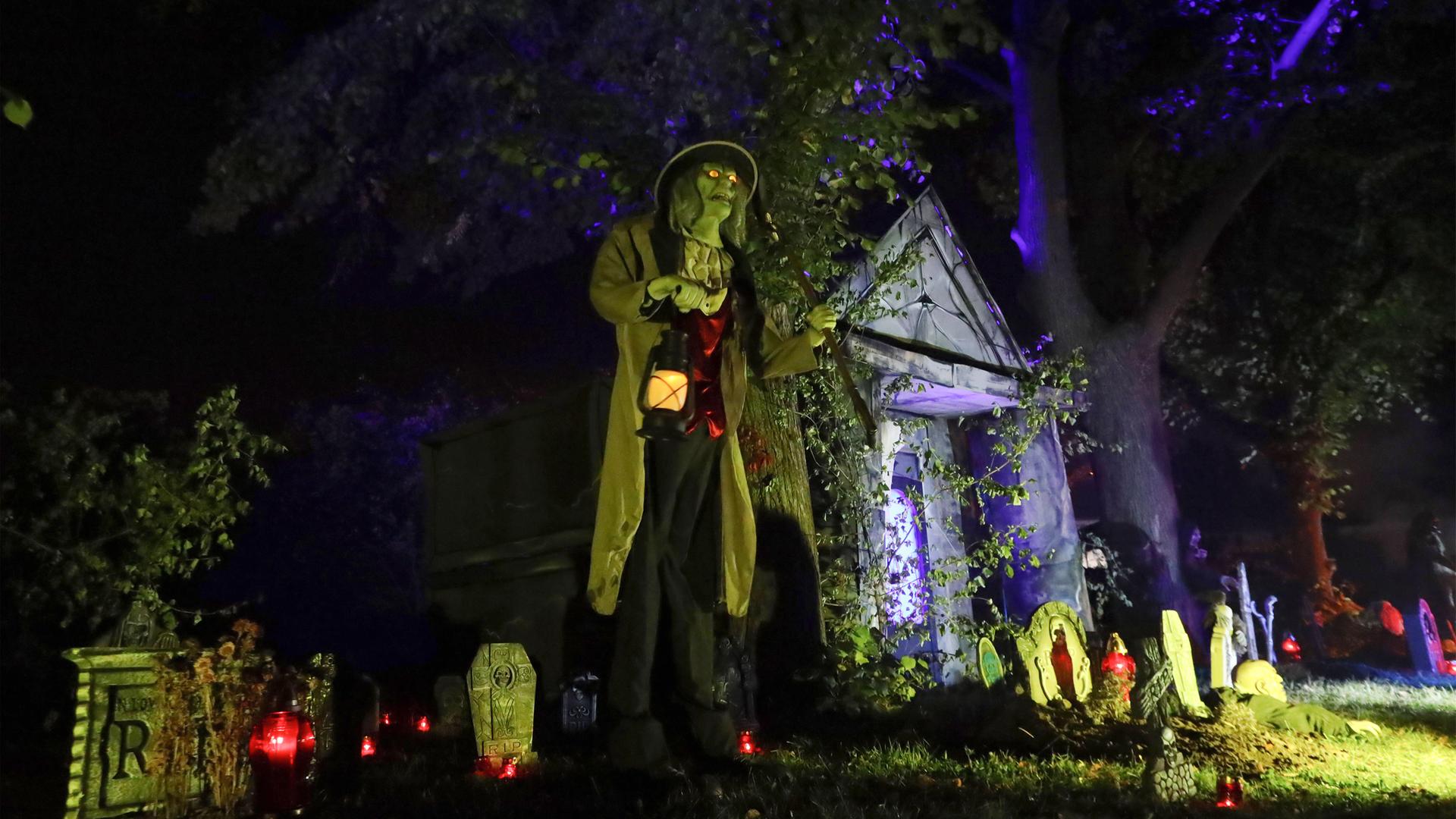 Helloween-Deko mit Geistern, Grabsteinen und einer Person mit Lampe