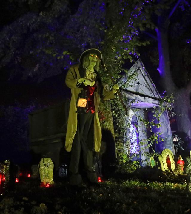 Helloween-Deko mit Geistern, Grabsteinen und einer Person mit Lampe