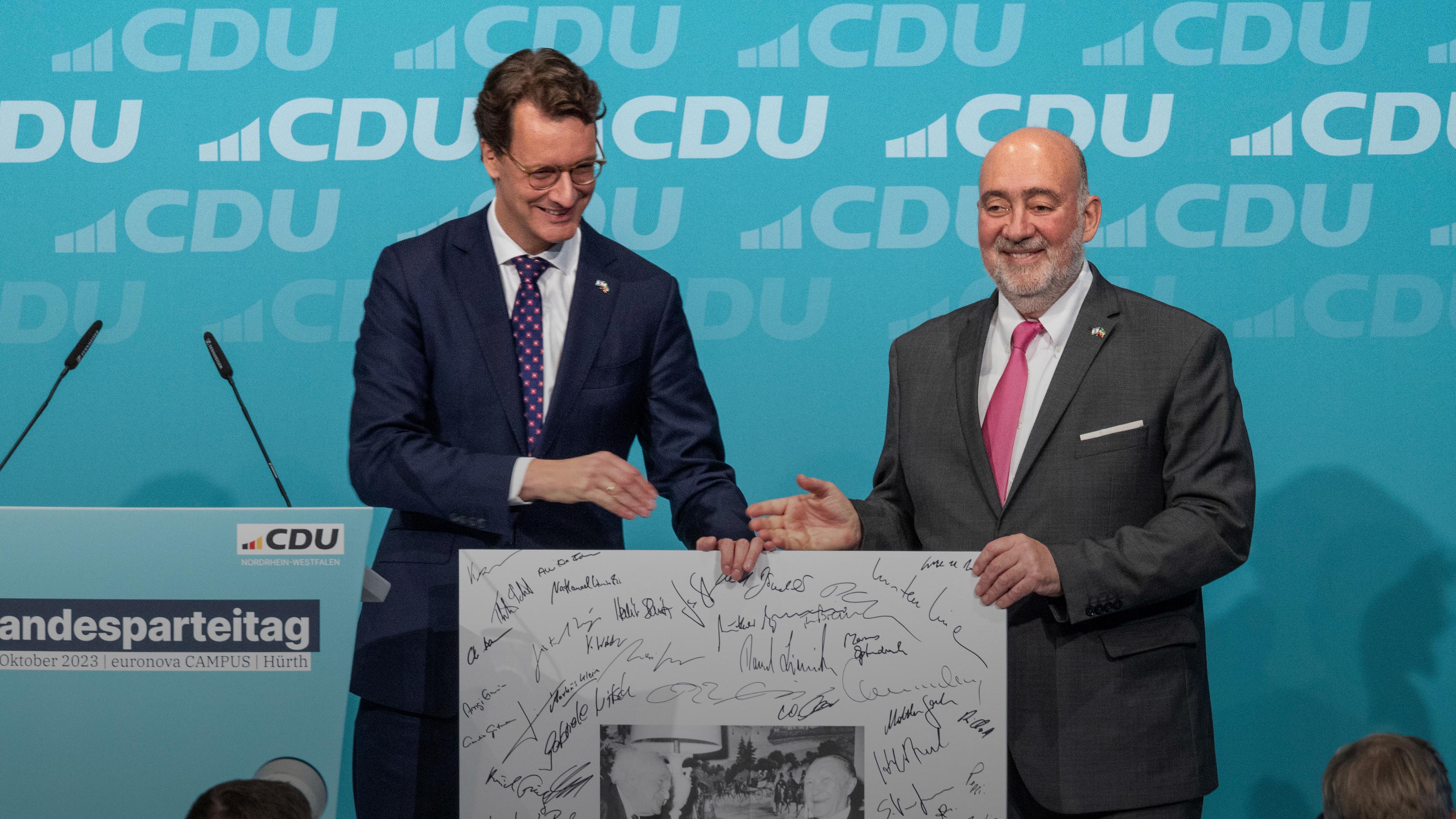 NRW-Ministerpräsident Hendrik Wüst (l.) überreicht dem israelischen Botschafter Ron Prosor beim CDU-Landesparteitag in Hürth eine Erinnerung zur Solidarität mit Israel.