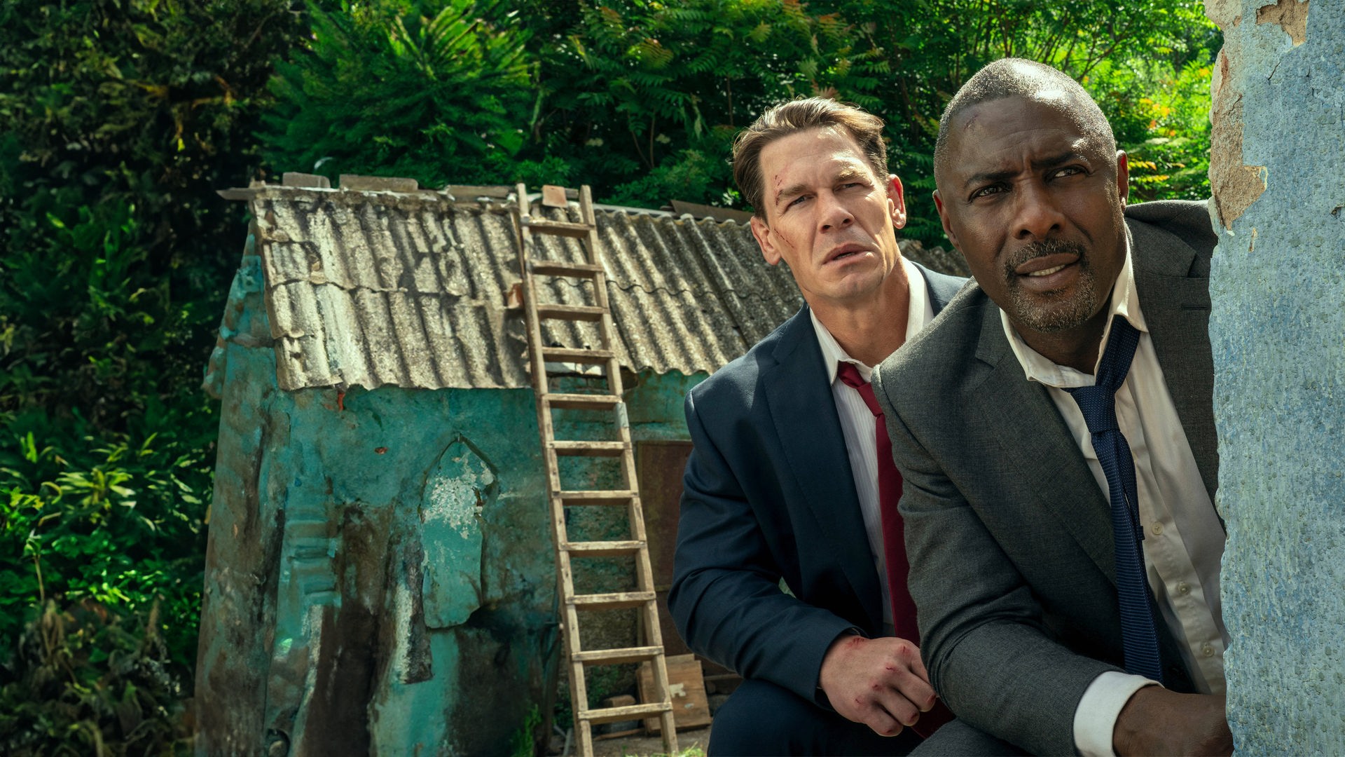 Will Derringer (John Cena) und Sam Clarke (Idris Elba) spähen um die Ecke einer Hauswand.