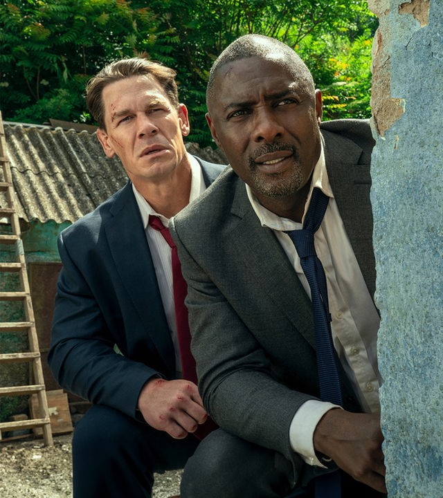 Will Derringer (John Cena) und Sam Clarke (Idris Elba) spähen um die Ecke einer Hauswand.