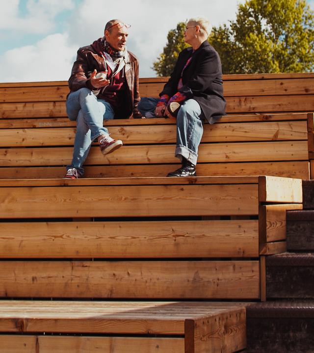 Protagonistin Lio sitzt mit ihrem Date auf Holzstufen unter blauem Himmel