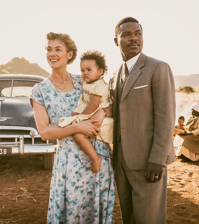 "A United Kingdom": Vor einem afrikanischen Dorf: Ruth Williams (Rosamund Pike) trägt ihre kleine Tochter auf dem Arm und steht neben Seretse Khama (David Oyelowo). Im Hintergrund steht ein Auto vor einer Hütte.