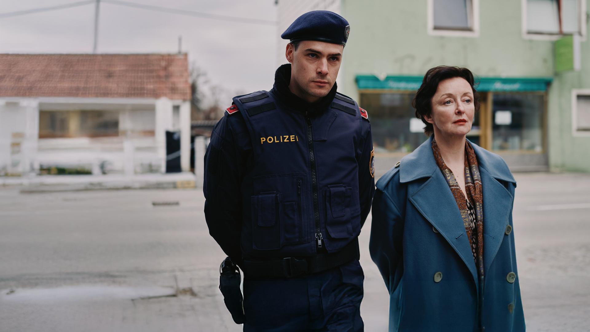 Patrick Brandl (Thomas Prenn, l.) und Marion Geyer (Regina Fritsch, r.) ermitteln in einem Mordfall. "ACHT - Ein Landkrimi": Patrick Brandl (Thomas Prenn) und Marion Geyer (Regina Fritsch) gehen zusammen die Straße entlang.
