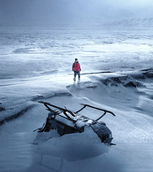 Arctic: In einer weiten, verschneiten Eislandschaft steht eine einzelne Person in roter Jacke zwischen den Wrackteilen eines Flugzeugs und eines Hubschraubers.