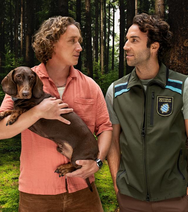 Mats trägt den Dackel Gustl auf dem Arm. Neben ihm steht Yascha.