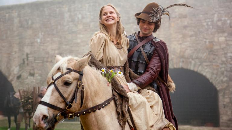 Vor dem Hintergrund der königlichen Burg sitzt Prinz Markus (André Kaczmarczyk), gekleidet wie ein Jäger, auf seinem weißen Pferd. Vor ihm, im Damensitz, Constanze (Sinja Dieks), die über das ganze Gesicht strahlt.