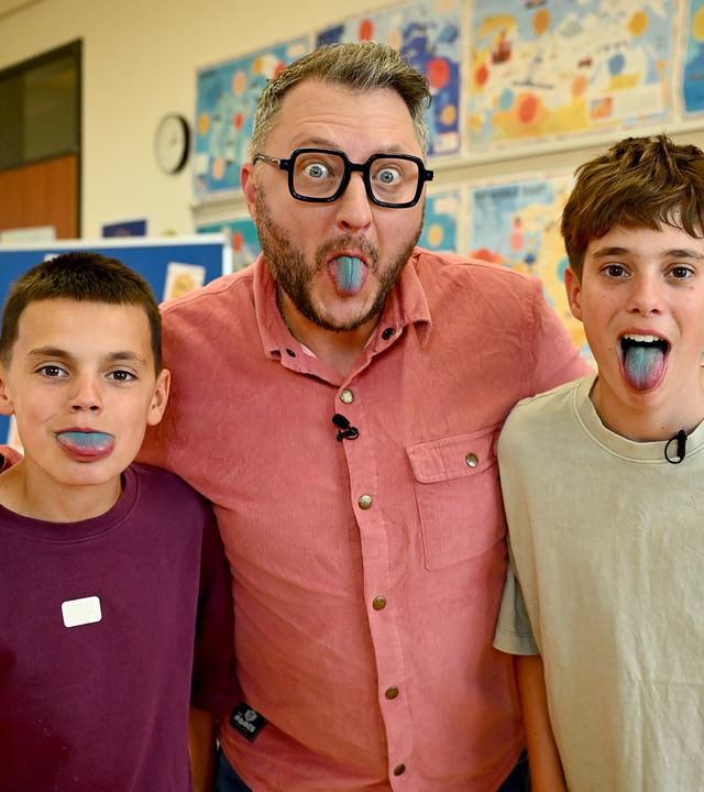 "besseresser Kids": Rejan, Sebastian Lege und Bruno (v. l. n. r.) stehen eng beieinander und strecken der Kamera ihre blau gefärbten Zungen entgegen. Im Hintergrund hängen bunte Poster. 
