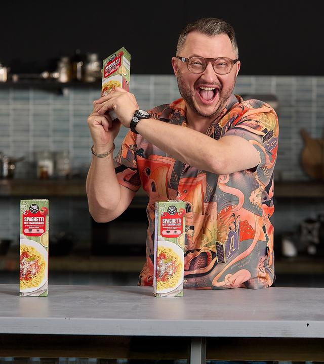  Sebastian Lege steht am Tresen seiner Werkstattküche. Vor ihm stehen zwei Packungen Spaghetti mit Tomatensoße.