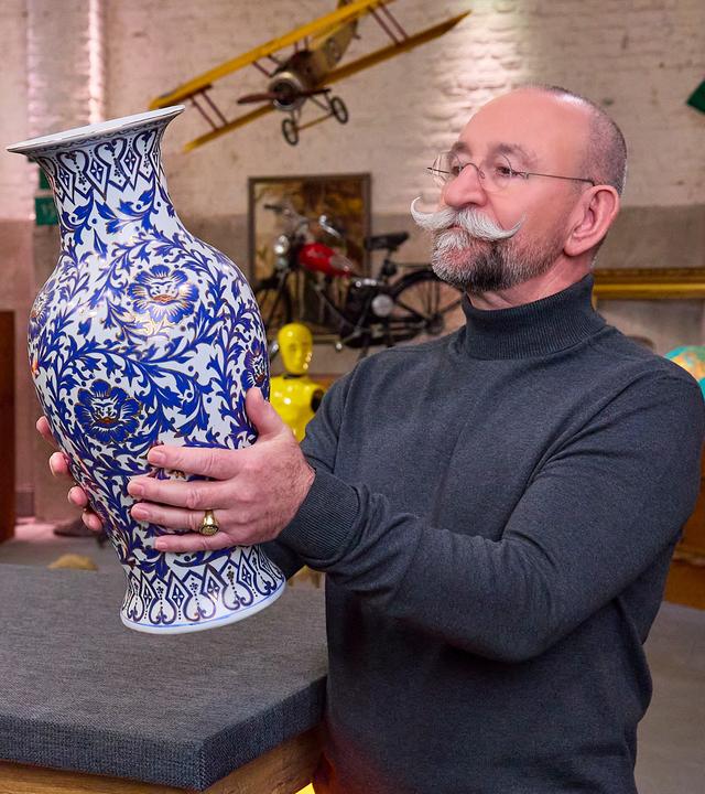 Horst Lichter steht im "Bares für Rares"-Studio und betrachtet eine Vase, die er in den Händen hält.