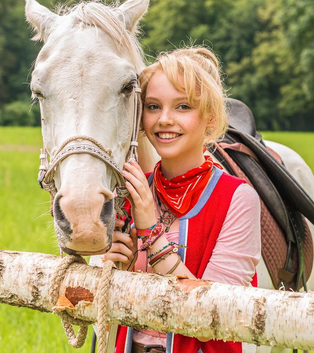 Bibi steht neben ihrem Pferd Sabrina und lächelt in die Kamera.