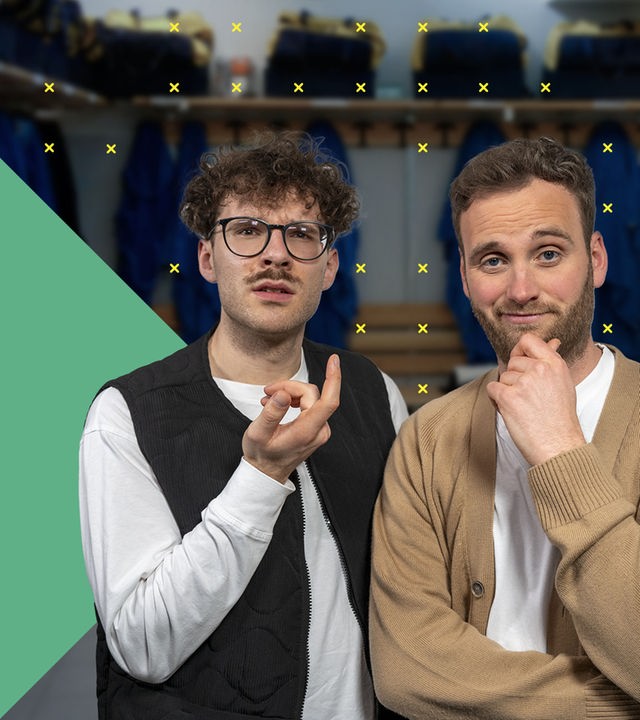 Dr. Leon Windscheid steht im Vordergrund und blickt nachdenklich in die Kamera. Neben ihm steht Max und gestikuliert. Im Hintergrund ist ein heller Raum mit Pflanzen und Möbeln zu sehen.