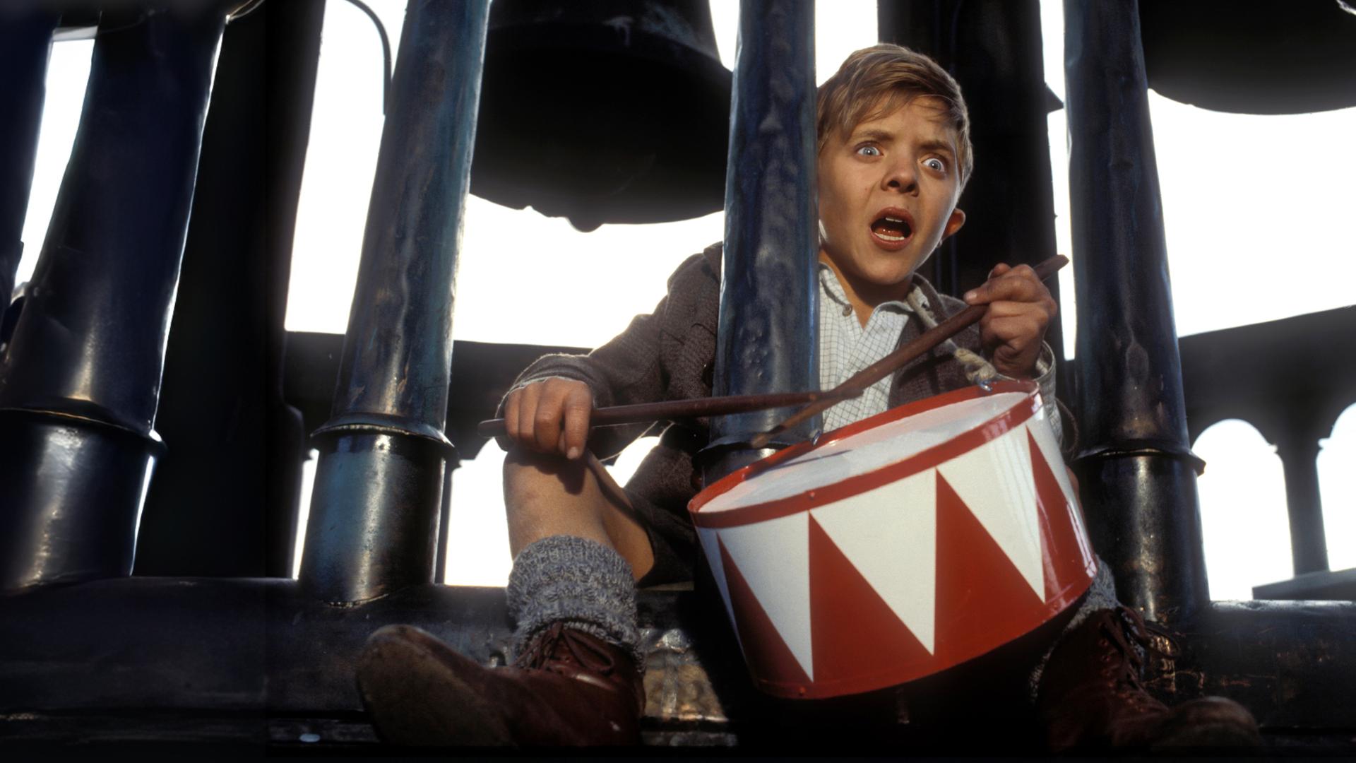 Mit vor Angst geweiteten Augen und offenem Mund sitzt der kleine Oskar Matzerath (David Bennent) auf der oberen Etage eines Glockenturms und trommelt auf seiner rot-weißen Blechtrommel.