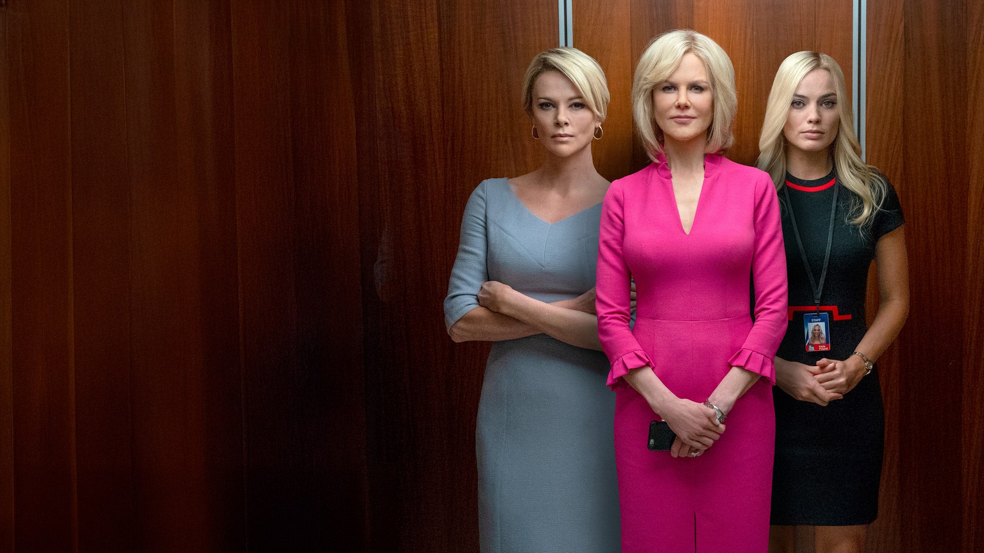 Gretchen Carlson (Nicole Kidman), Megyn Kelly (Charlize Theron) und Kayla Pospisil (Margot Robbie) stehen nebeneinander in einem offenen Fahrstuhl und blicken den Betrachter an. Gretchen Carlson trägt ein auffälliges, pinkfarbenes Kleid.