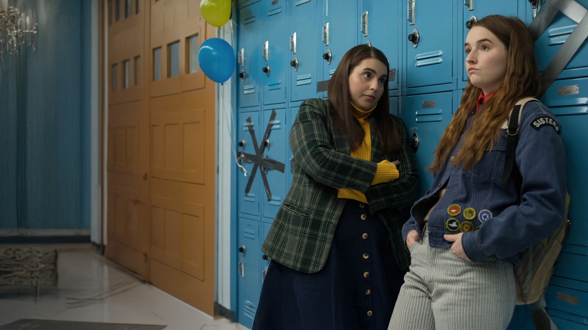Molly (Beanie Feldstein) und Amy (Kaitlyn Dever) stehen nebeneinander vor den blauen Schulspinden in ihrer Highschool. Sie unterhalten sich und sehen nachdenklich und genervt aus.