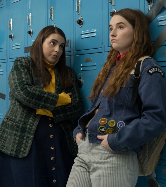 Molly (Beanie Feldstein) und Amy (Kaitlyn Dever) stehen nebeneinander vor den blauen Schulspinden in ihrer Highschool. Sie unterhalten sich und sehen nachdenklich und genervt aus.