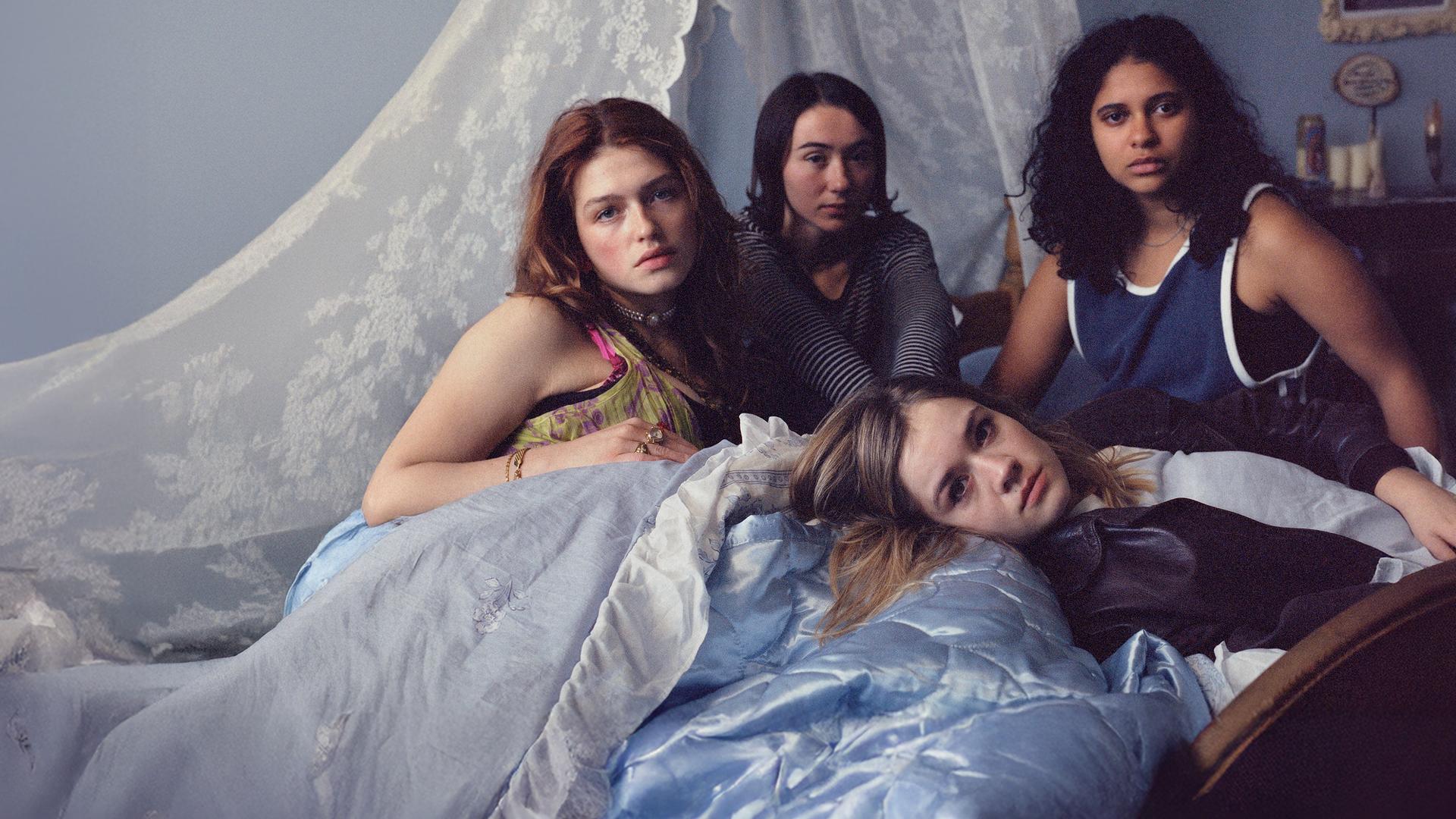 Victoria (Sonja Weißer), Malou (Zoe Stein), Katharina (Lea Drinda) sitzen auf einem mit Spitze dekorierten Bett, während Ricky (Safinaz Sattar) liegt.