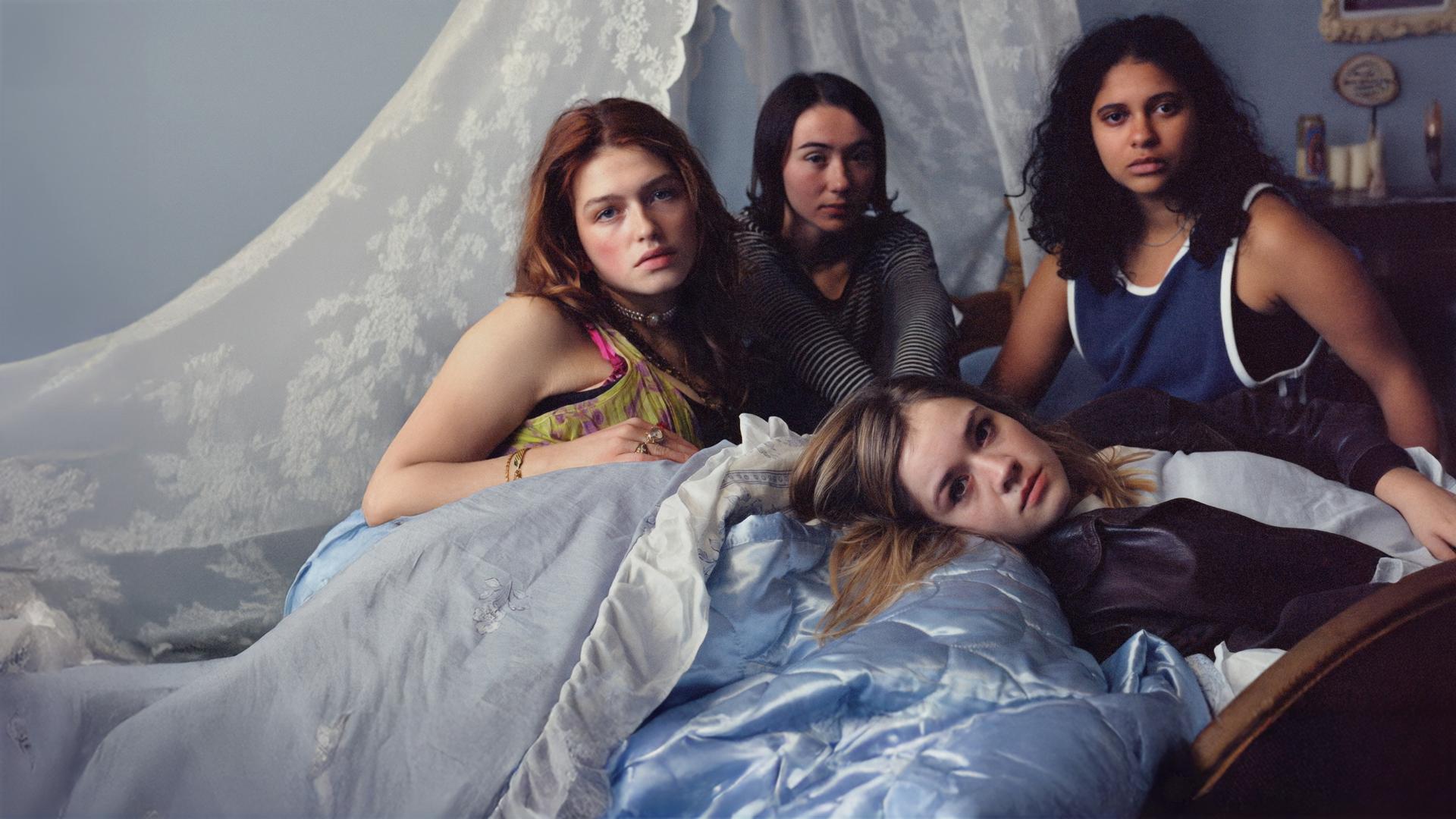 Victoria (Sonja Weißer), Malou (Zoe Stein), Katharina (Lea Drinda) sitzen auf einem mit Spitze dekorierten Bett, während Ricky (Safinaz Sattar) liegt.