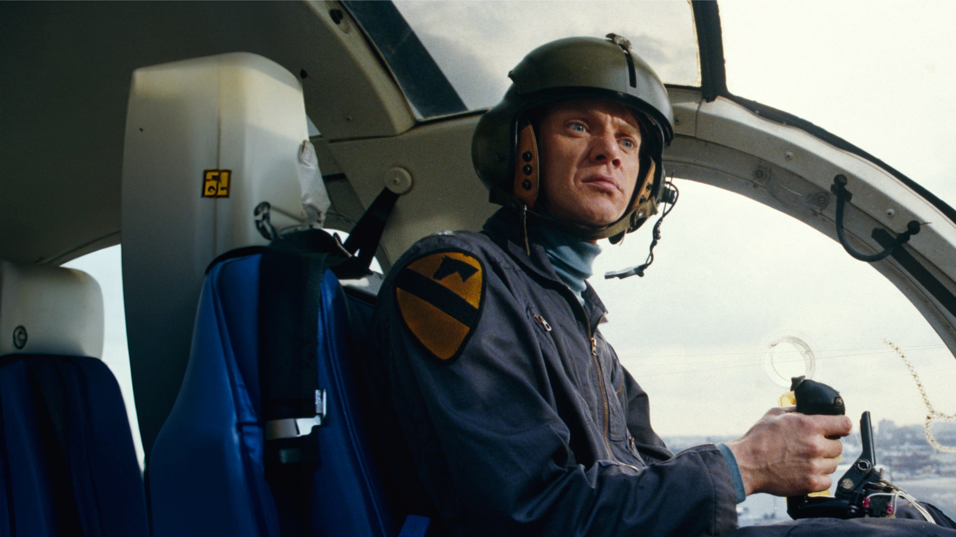 Colonel F. E. Cochrane (Malcom McDowell) sitzt im Cockpit eines Hubschraubers und blickt ernst zur Seite.