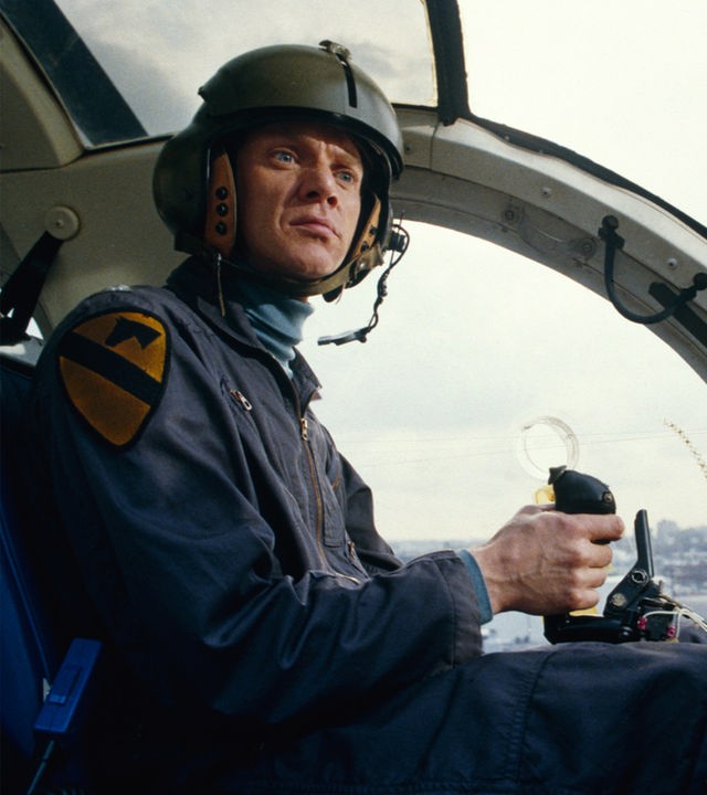 Colonel F. E. Cochrane (Malcom McDowell) sitzt im Cockpit eines Hubschraubers und blickt ernst zur Seite.