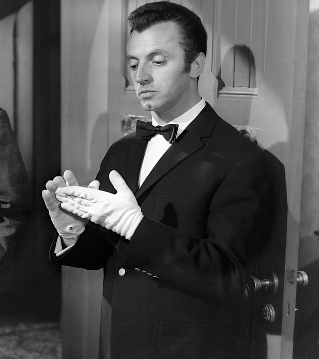 Der Anwalt Frank Tanner (Heinz Drache, links) hält eine Art hölzernes Möbelstück in der Hand, während er mit dem Butler Bonwit (Eddy Arendt) spricht, der sich gerade die weißen Handschuhe glattstreicht.