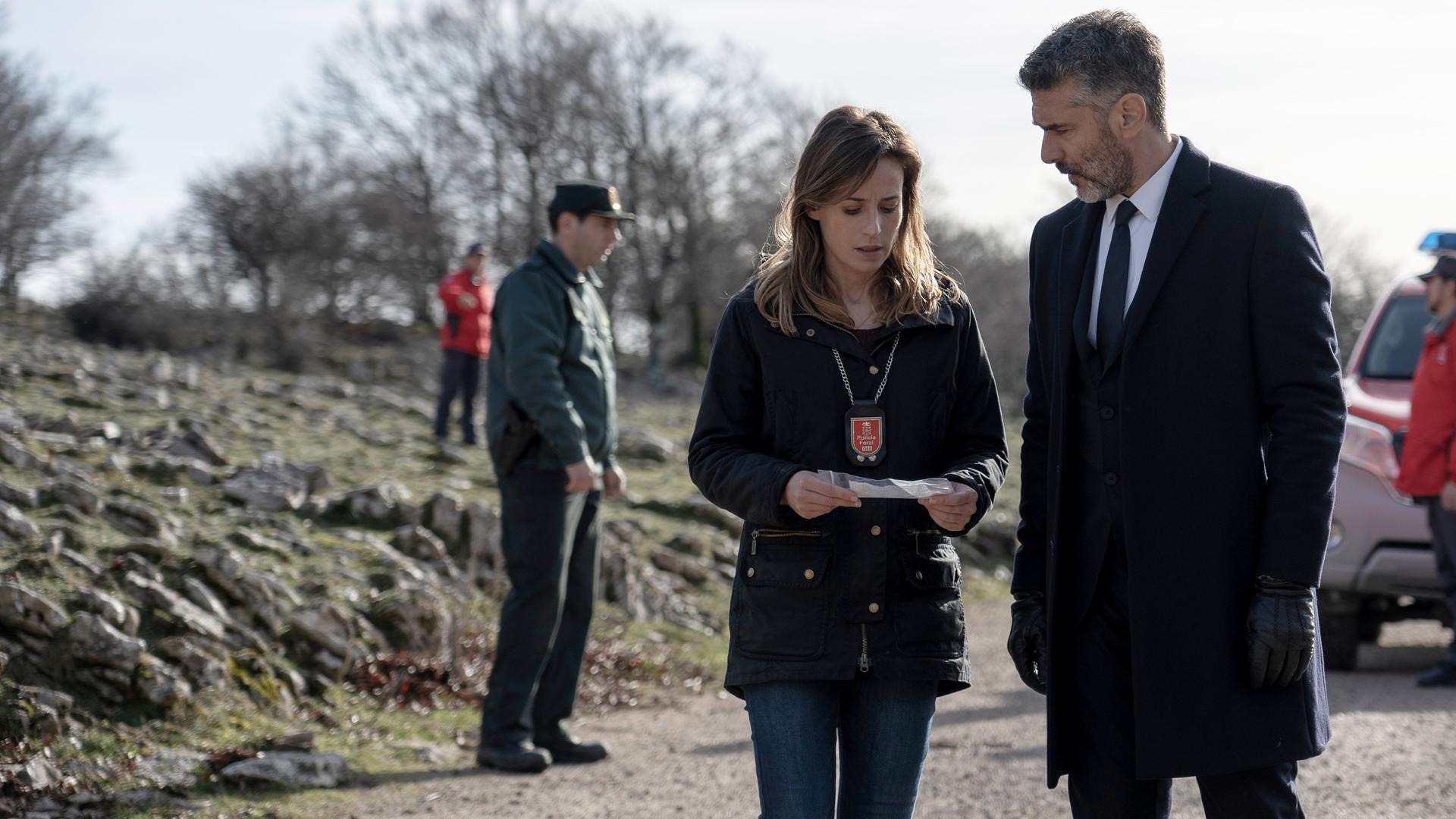Richter Juez Markina (Leonardo Sbaraglia, r.) wird für Kommissarin Amaia Salazar (Marta Etura, l.) zu einem Vertrauten und Verbündeten. "Das Tal der vergessenen Kinder": Javier Markina (Leonardo Sbaraglia) steht neben Kommissarin Amaia Salazar (Marta Etura) auf einem Schotterweg. Sie hält ein Dokument in den Händen.