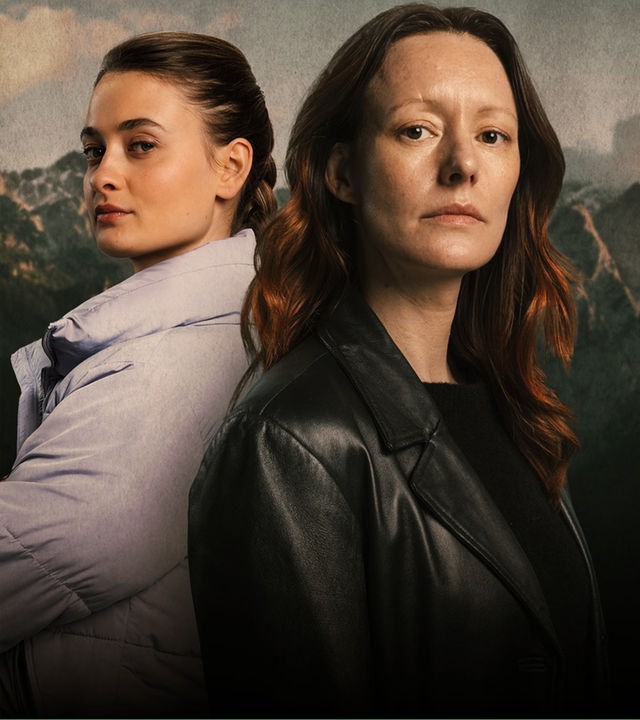 Ex-Kommissarin Ira Zach (Lavinia Wilson) und ihre junge Nachfolgerin Daphne Meindl (Philine Schmölzer) stehen Rücken an Rücken, vor der Bergkulisse von Garmisch-Partenkirchen.