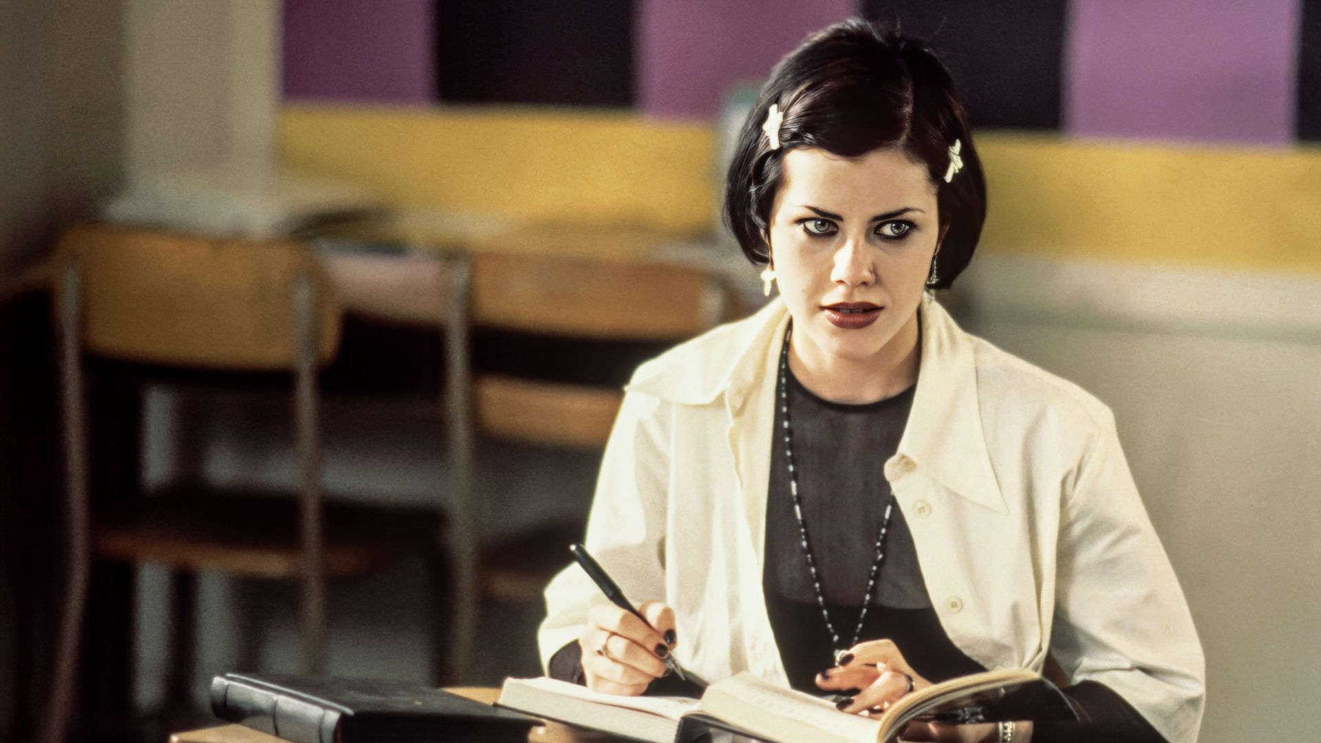 Nancy (Fairuza Balk) sitzt mit einem Stift in der Hand an einem Schultisch, auf dem mehrere Bücher liegen.