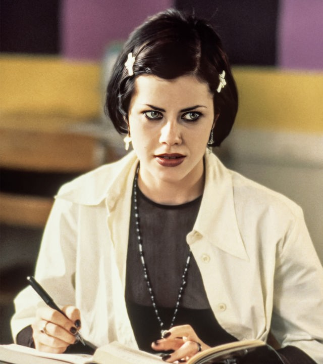 Nancy (Fairuza Balk) sitzt mit einem Stift in der Hand an einem Schultisch, auf dem mehrere Bücher liegen.