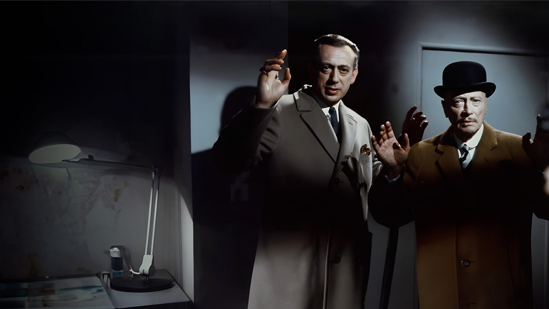 Inspektor Perkins (Horst Tappert) und Sir Arthur (Hubert von Meyerinck) stehen mit erhobenen Händen nebeneinander in einem düsteren Raum und blicken ernst, während eine Waffe bedrohlich auf sie gerichtet ist.