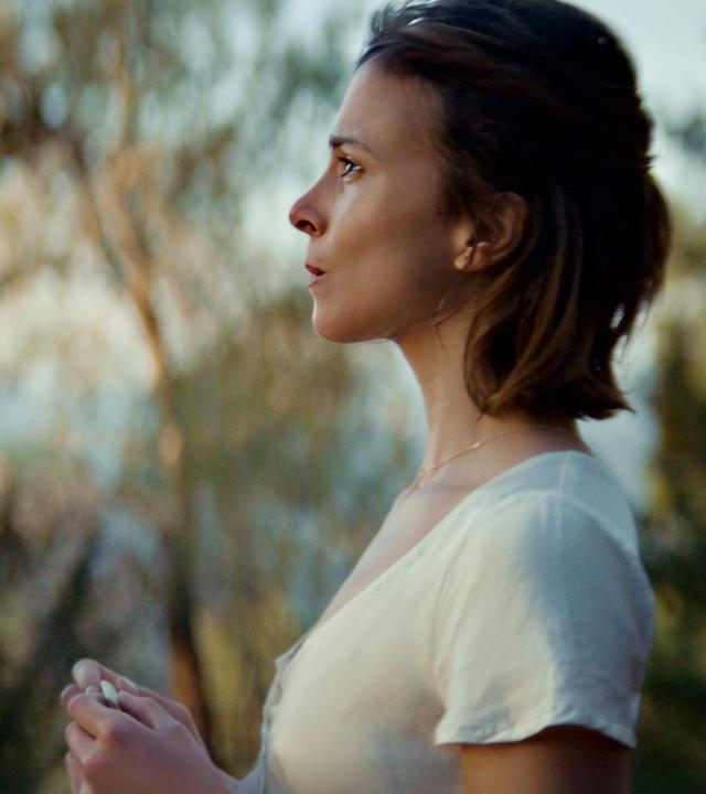 Mascha (Aylin Tezel) in einer seitlichen Aufnahme: Sie steht gedankenverloren vor einer Birke.