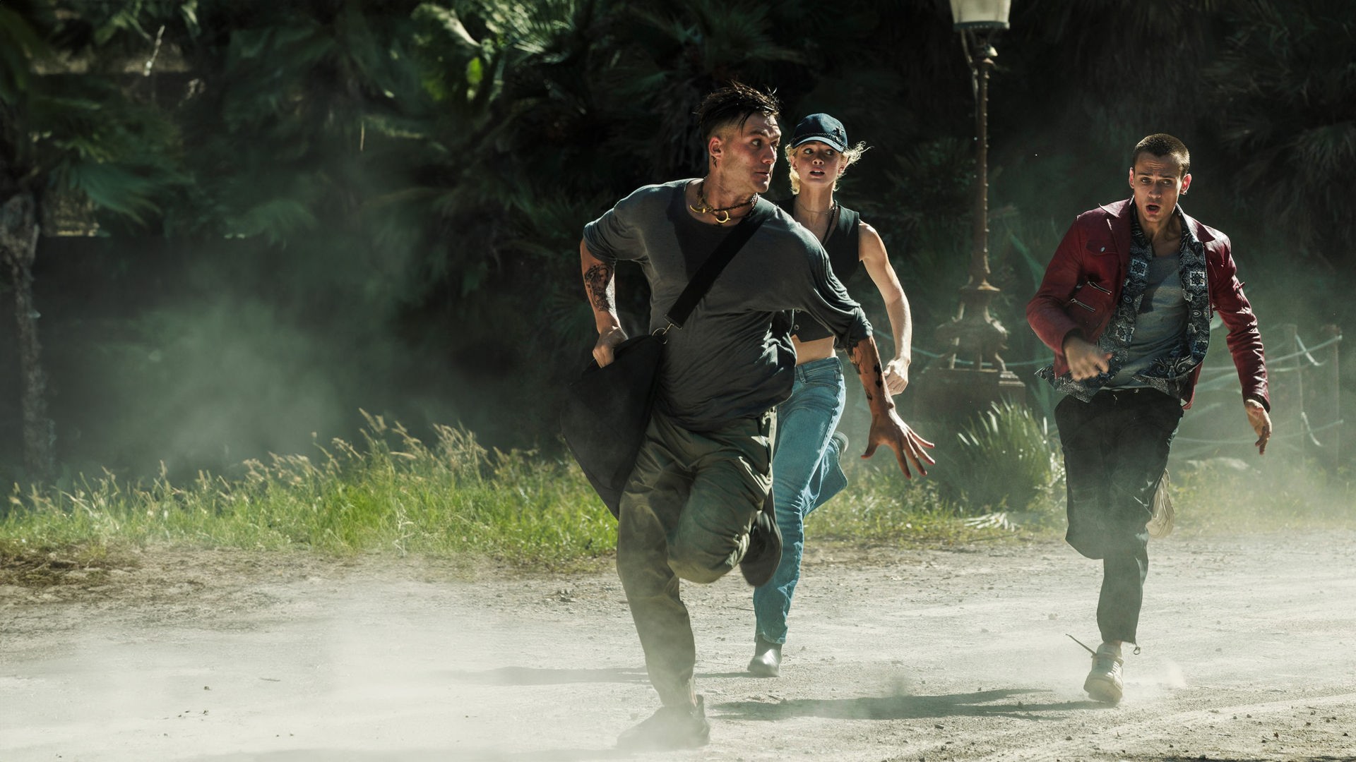 "Die letzte Nacht in Palermo": Halbtotale: Komandante (Lorenzo Richelmy) ist verschwitzt, trägt eine schwarze Sporttasche und rennt vorneweg auf einer staubigen Straße durch einen Park. Ihm folgen Sophie (Elena Kampouris) und Giulio (Saul Nanni). 