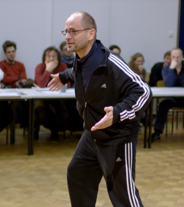 "Die Prüfung": Ein Mann im Trainingsanzug führt eine ausladende Bewegung vor mehreren Zuschauern vor.