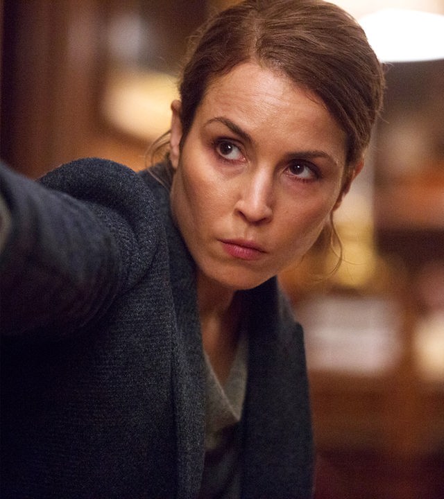 Alice Racine (Noomi Rapace) steht neben einem Türrahmen und zielt mit ihrer Pistole.